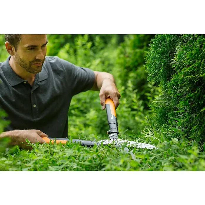 Fiskars Getriebe-Heckenschere Powergear X HSX 92 - Länge: 63 cm - Mann schneidet eine Hecke mit einer Fiskars Heckenschere. Die Heckenschere hat orangefarbene Griffe und scharfe Klingen für präzise Schnitte.