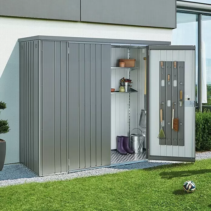 Biohort Geräteschrank 230 - Quarzgrau - Grauer Metall-Geräteschuppen mit offener Tür, zeigt Regale und Gartengeräte, im Freien neben einem Gebäude.