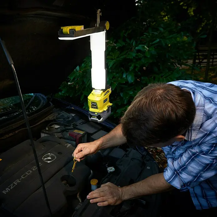 Ryobi ONE+ LED-Arbeitsleuchte - 18 V, Li-Ionen, Ohne Akku - Ein Mann prüft den Ölstand seines Autos mit einer Ryobi Arbeitsleuchte, die für optimale Sicht sorgt.