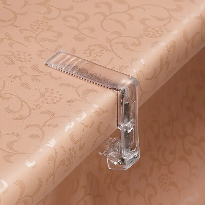 D-c-fix Tischdeckenhalter - Glasklar, 4 Stk. - Nahaufnahme einer Tischdeckenklammer aus Kunststoff auf einem Tisch mit Blumenmuster.