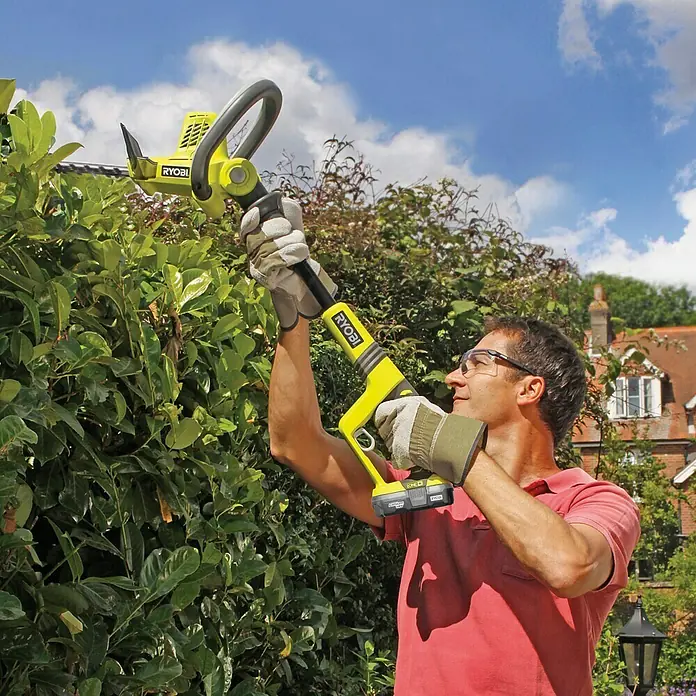 Ryobi ONE+ Maschinenpaket - Akku-Heckenschere OHT1850X,18V, 4 Ah Akku & 2A Ladegerät - Ein Mann schneidet eine Hecke mit einer gelben Ryobi Akku-Heckenschere.