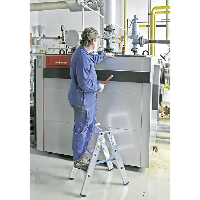 Krause Stabilo Doppelleiter - Anzahl Tritte: 6 Stk., Arbeitshöhe: 2,25 m, Aluminium - Handwerker auf einer Krause Leiter, der an einer großen Heizanlage arbeitet, mit Rohrzange in der Hand.