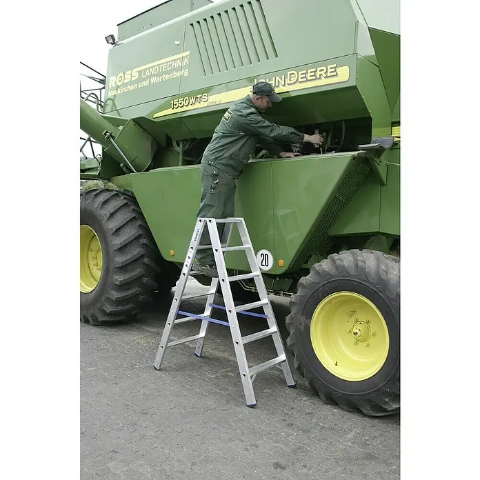 Krause Stabilo Doppelleiter - Anzahl Tritte: 12 Stk., Arbeitshöhe: 2,95 m, Aluminium - A man is on a KRAUSE folding ladder, working on a John Deere combine.
