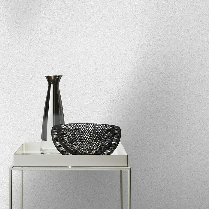 Rasch Papiertapete Aderstruktur - Weiß, Uni, 10,05 x 0,53 m - Dekorative Anordnung mit einer schlanken Vase und einer filigranen Schale auf einem modernen Beistelltisch vor einer strukturierten Wand.