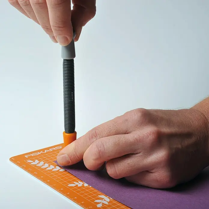 Fiskars Ösenstanzer - 2 -tlg. - Eine Nahaufnahme einer Fiskars Schneidemaschine, die von zwei Händen bedient wird, um präzise Schnitte auf einer lila Papieroberfläche zu erzielen.