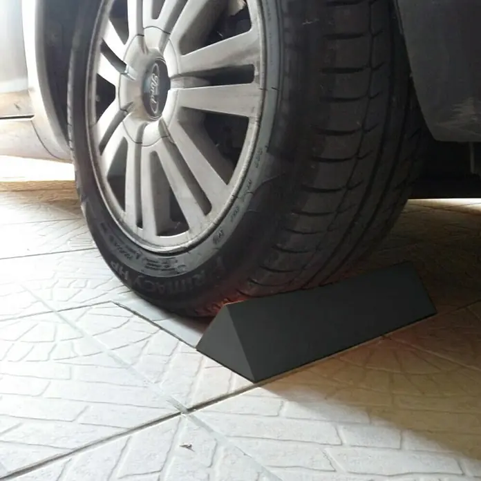 Cuña para ruedas adhesiva - Apto para: Vehículos, 1 ud. - Una cuña negra, utilizada como calzo de rueda, se coloca debajo de un neumático Ford sobre baldosas para evitar que el coche ruede.