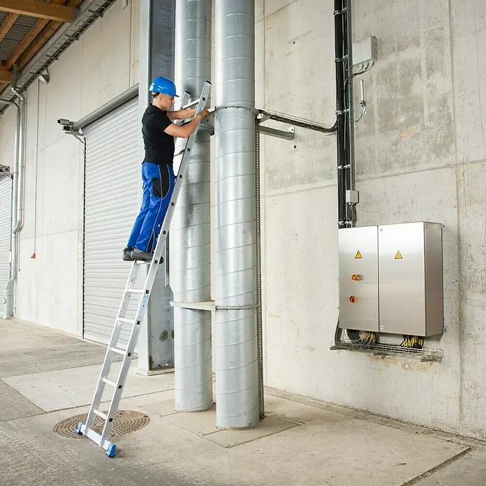 Krause Stabilo Anlegeleiter - Anzahl Tritte: 12 Stk., Arbeitshöhe: 4,4 m, Aluminium - Ein Mann auf einer Leiter, der an zwei silbernen Rohren arbeitet, mit Fokus auf die vielseitige Leiter für sichere Höhe.