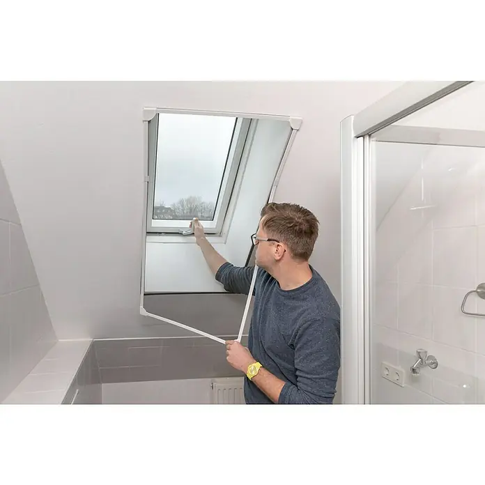 Schellenberg Insektenschutz-Dachfenster Magnetic - B x H: 80 cm x 140 mm, Weiß, Montage Insektengitter: Magnetisch anheften - Mann befestigt ein Insektenschutzgitter an einem Dachfenster. Das Gitter ist weiß und hat eine rechteckige Form, um Insekten fernzuhalten.