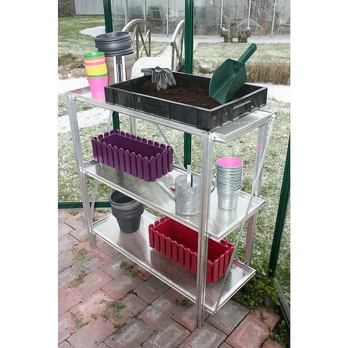 KGT Gewächshaus-Regal Universal - 110 x 35 x 100 cm, Metall - Ein dreistufiges Regalsystem im Gewächshaus, beladen mit Töpfen, Pflanzkästen und Gartengeräten, ideal für die Pflanzenanzucht.