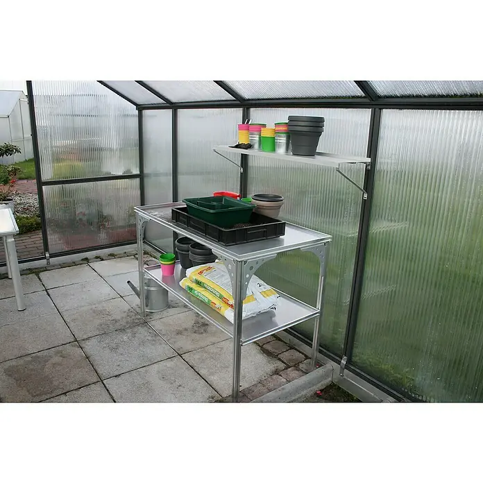 KGT Gewächshaus-Tisch - 121 x 64 x 80 cm - Das Bild zeigt einen silbernen Arbeitstisch mit zwei Regalen und einer Ablagefläche in einem Gewächshaus. Auf dem Tisch befinden sich Töpfe, Erde und Werkzeuge.