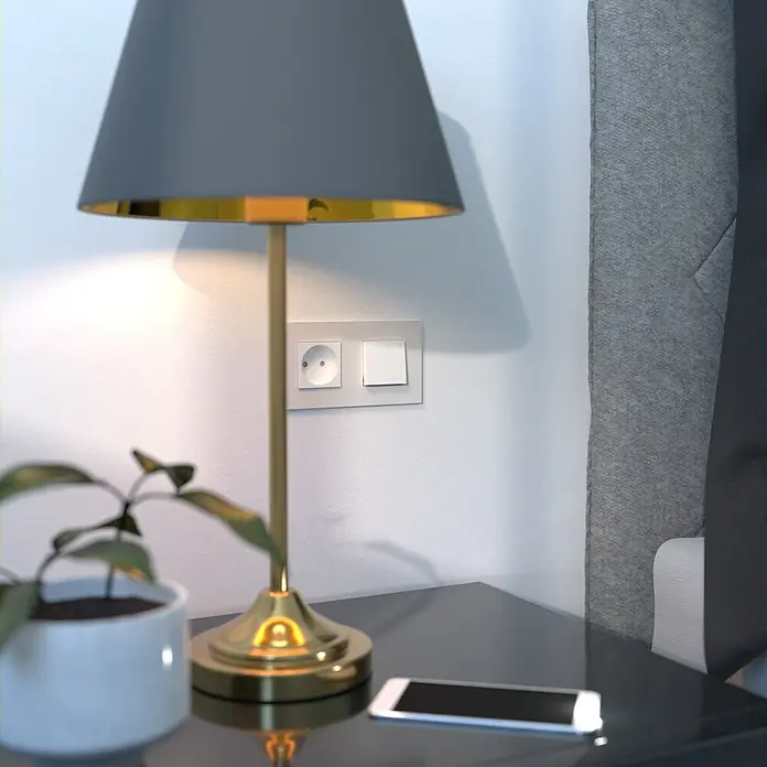 Schneider Electric New Unica Marco - Beige, Modelo de mecanismos: x 2, Plástico, Instalar - Primer plano de una lámpara de noche con pantalla gris, detalles dorados y un smartphone sobre una mesita de noche oscura.