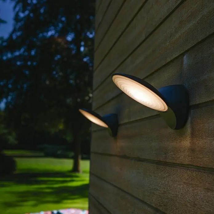 Lutec Aplique exterior LED Tona - 9 W, 19 x 18 x 14,1 cm, Antracita, Opal, IP44 - Dos modernas lámparas de pared para exteriores iluminan el jardín y la fachada con estilo sobre una pared de madera.