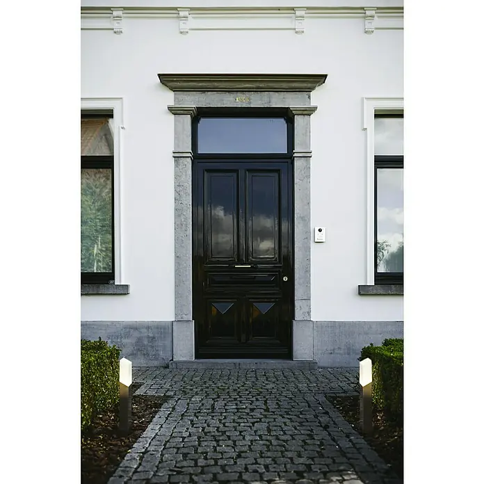 Lutec Sobremuro exterior Flat - 8 W, 5 x 10 x 45 cm, Con bombillas - Entrada con una elegante puerta principal negra, enmarcada en piedra, con un camino empedrado y elegantes luces modernas.