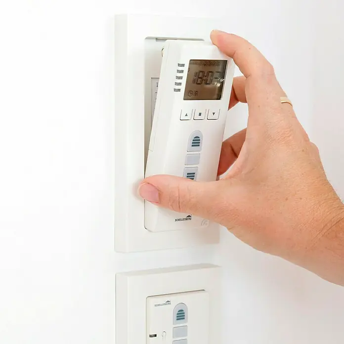 Schellenberg Temporizador Premium - L x An x Al: 28,5 x 11 x 5,5 cm, Blanco, En pared - Primer plano de una mano que instala un temporizador Schellenberg en una pared blanca.