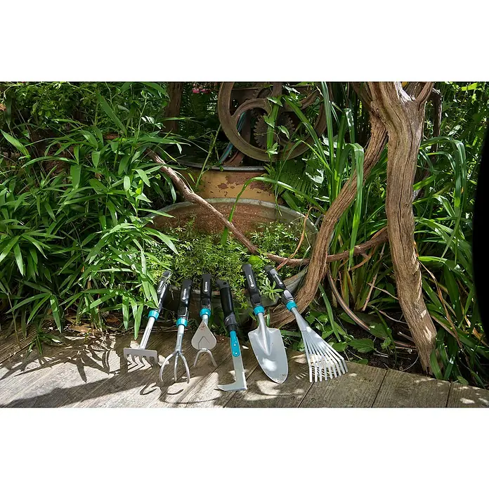 Gardena Comfort Hand-Fugenkratzer - Stahl - Gartengeräte-Set von Gardena, bestehend aus Harke, Grubber, Unkrautstecher, Hacke, Schaufel und Rechen, vor üppigem Grün.