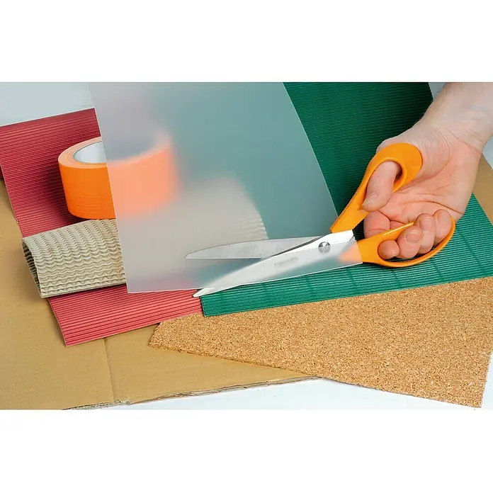 Fiskars Tijera universal Premium - Largo: 25 cm, Acero inoxidable - Primer plano de unas tijeras naranjas cortando una lámina de acetato, con materiales de manualidades como cartón y papel de colores.