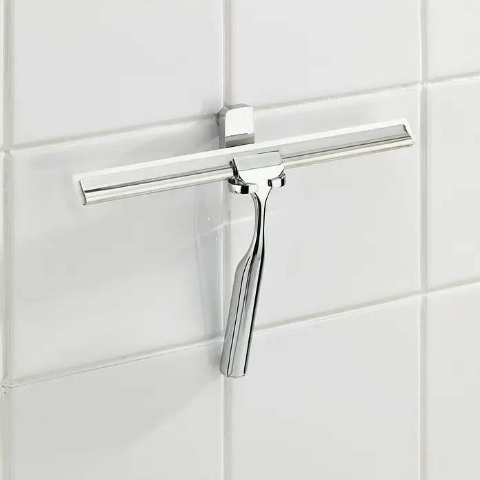 Wenko Limpiamamparas para baño y ducha Premium - Cromo - Primer plano de un limpiacristales de ducha cromado montado sobre azulejos blancos, asegurando una mampara limpia y brillante.