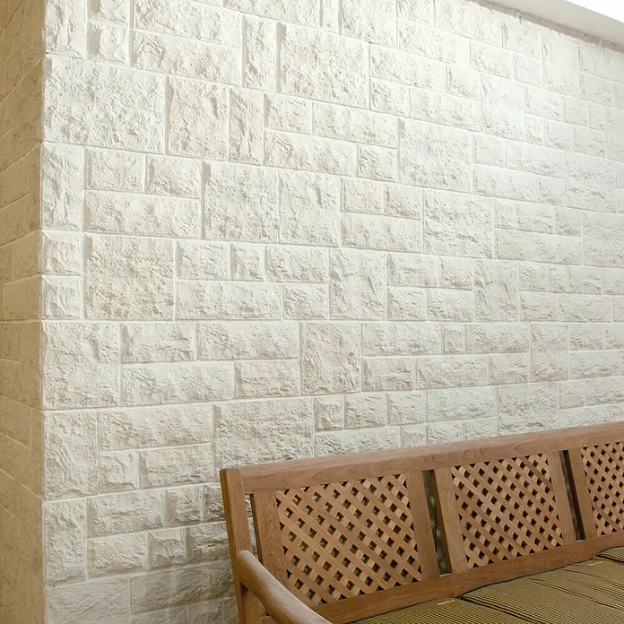 Revestimiento de piedra Travertino Split - Beige, Cantidad total: 4 pzs. - Primer plano de una pared con paneles decorativos de ladrillo blanco y un banco de madera delante, creando un ambiente cálido y acogedor.
