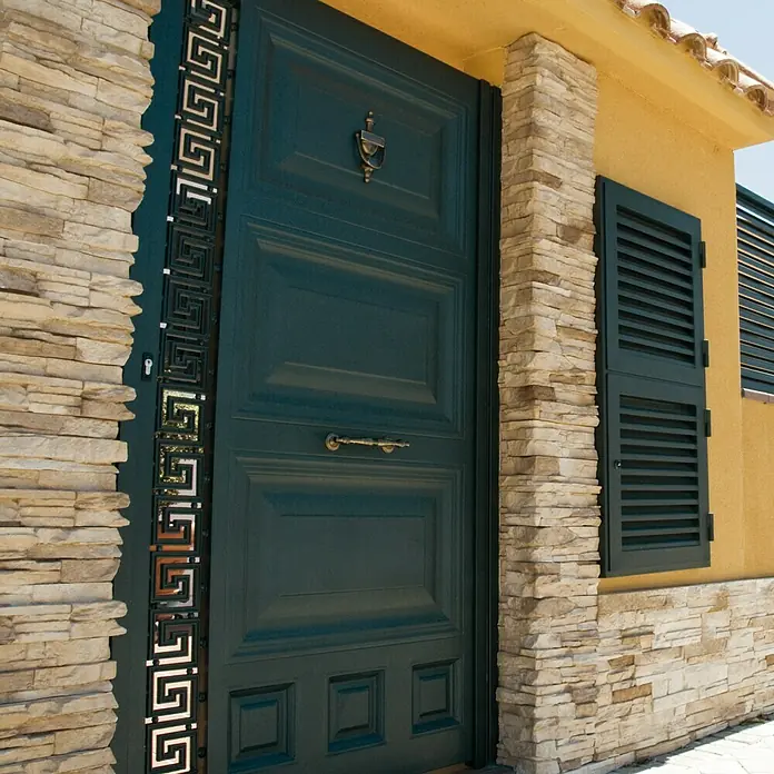 Revestimiento de piedra Petra Arena - Cantidad total: 4 pzs., Arena - Imagen de una elegante puerta principal verde con detalles decorativos y un llamador dorado, enmarcada en una pared de piedra.