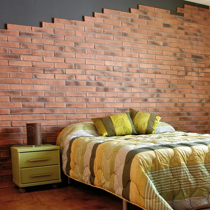 Revestimiento de piedra Mediterráneo Teja - 24 x 5,5 x 2,5 cm - Dormitorio con una llamativa pared de ladrillo y una cama acogedora con ropa de cama de color amarillo verdoso. Una mesita de noche junto a la cama.