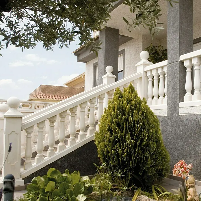 Pasamano Roma - Hormigón - Primer plano de una elegante balaustrada blanca que conduce a una casa, rodeada de exuberante vegetación. Un hermoso punto focal para cualquier amante del jardín.