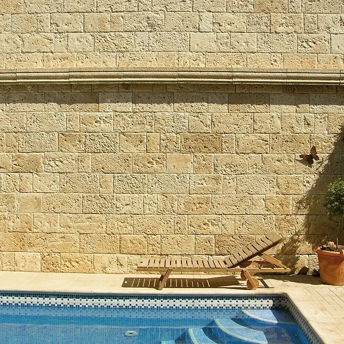 Revestimiento de piedra Coral Piedra - Coral - La imagen muestra una tumbona de madera junto a una piscina decorada con mosaico azul, invitando a relajarse y disfrutar.
