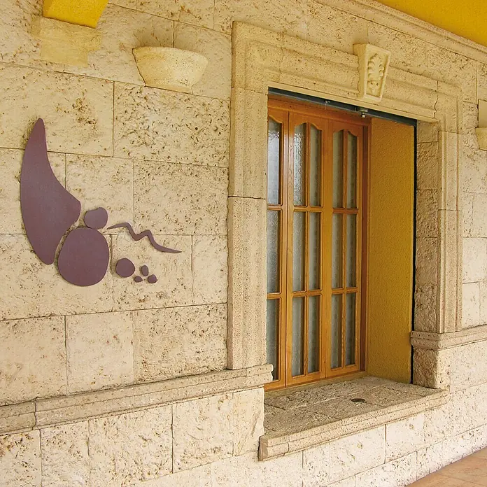 Revestimiento de piedra Coral Piedra - Coral - Primer plano de una pared de piedra clara con una obra de arte mural abstracta moderna y una ventana con marco de madera.