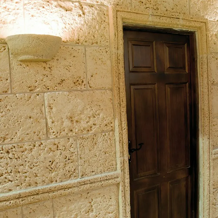 Revestimiento de piedra Coral Piedra - Coral - Primer plano de una puerta de madera con accesorios antiguos, incrustada en una pared de piedra con iluminación decorativa.