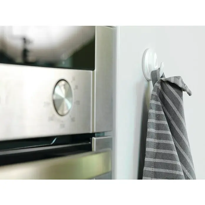Tesa Powerstrips Gancho autoadhesivo Mini Redondo - Blanco - Un paño de cocina gris a rayas cuelga de un gancho blanco junto a un horno moderno. Accesorios útiles en la cocina.