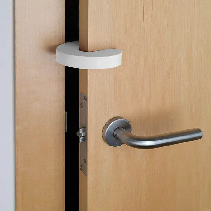 Inofix Tope de puerta 5200-2 - Blanco - Primer plano de una puerta con un tope de puerta de espuma, que evita que los dedos queden atrapados. También hay un pomo plateado en la imagen.