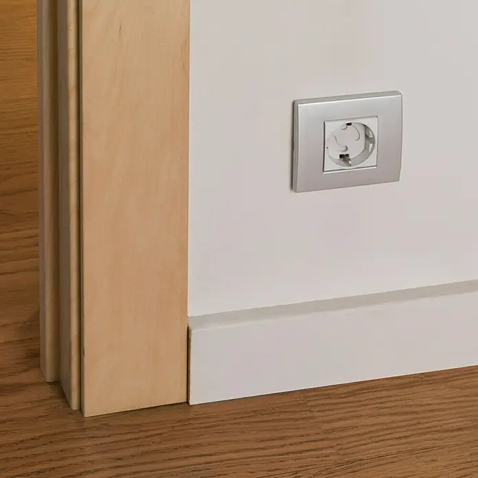 Inofix Protector de enchufe 5400-2 - Blanco, 6 ud. - Vista detallada de una toma de corriente plateada en una pared blanca, junto a un marco de puerta de madera, destacando las líneas limpias.