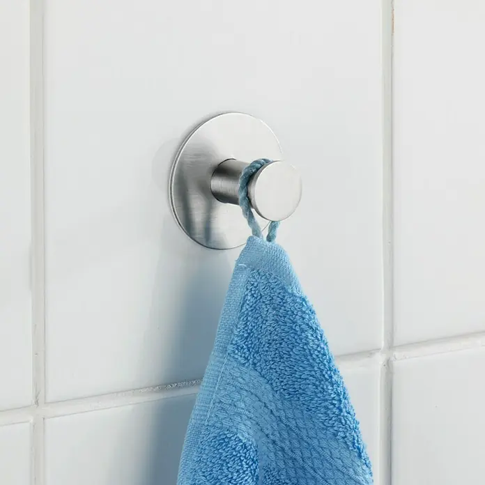 Wenko Handtuchhaken Celano - 1 Stk., Edelstahl, Matt - Ein silberner Handtuchhaken mit einem blauen Handtuch hängt an einer weißen, gefliesten Wand im Badezimmer.