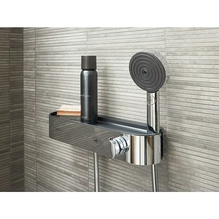 Hansgrohe Pulsify Select S Handbrause 105 Relaxation EcoSmart - Anzahl Funktionen: 3 Stk., Durchmesser: 10,5 cm, Chrom - Nahaufnahme eines Hansgrohe Duschsystems mit Ablage, Shampoo und Bürste vor einer grauen Wand.