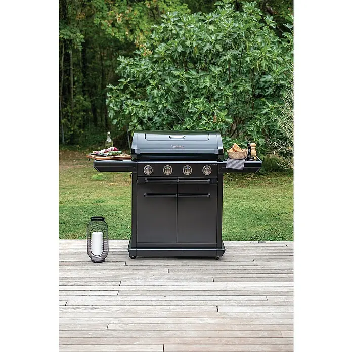 Campingaz Barbacoa de gas Onyx Premium - Superficie de la parrilla (An x Pr): 61 x 46 cm, 3,4 kW, Número de quemadores: 4 - Foto de una barbacoa de gas Campingaz negra con cuatro quemadores en el exterior, con estantes laterales y un armario de almacenamiento en una terraza de madera.