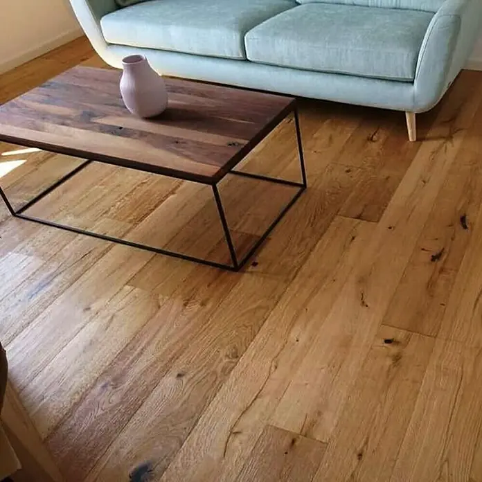 Parkett - Eiche Antik Laax, Landhausdiele, 1.900 x 190 x 15 mm - Ein rechteckiger Couchtisch aus dunklem Holz mit einem schwarzen Metallgestell steht auf einem Holzboden. Eine Vase steht auf dem Tisch.