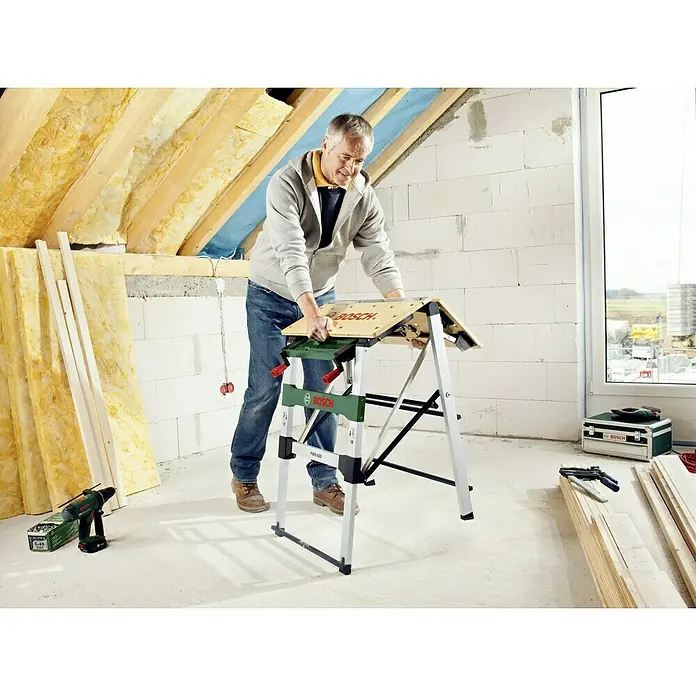 Bosch Werkbank PWB 600 - L x B: 680 x 680 mm, Arbeitshöhe: 834 mm, Belastbarkeit: 200 kg - Ein Mann bedient eine Bosch PWB 600 Werkbank. Sie ist grün, schwarz und silberfarben und bietet eine stabile Arbeitsfläche für Heimwerkerprojekte.