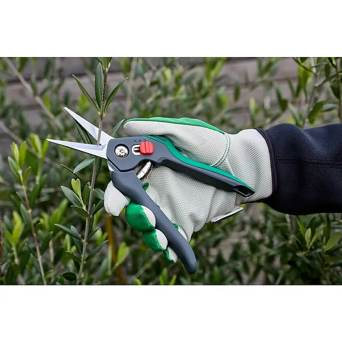 Gardol Comfort Trimmschere GDB12 - Bypass, Max. Aststärke: 12 mm - Nahaufnahme einer Hand mit Gartenhandschuh, die eine Gartenschere hält, um einen kleinen Zweig zu schneiden.