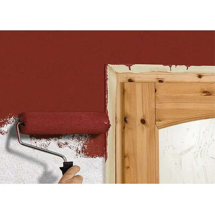 Tesa Cinta de pintor Standard - 50 m x 25 cm - Una pared está siendo pintada de rojo con un rodillo de pintura, junto a un borde de madera protegido con cinta de pintor.