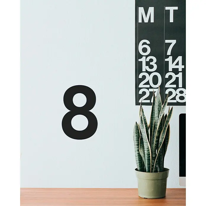 Vinilo de pared Número 8 - 4 x 9 cm, Negro, Plástico - Primer plano de una planta de interior en maceta, con un calendario y el número ocho en la pared. Añade calma y decoración al espacio.