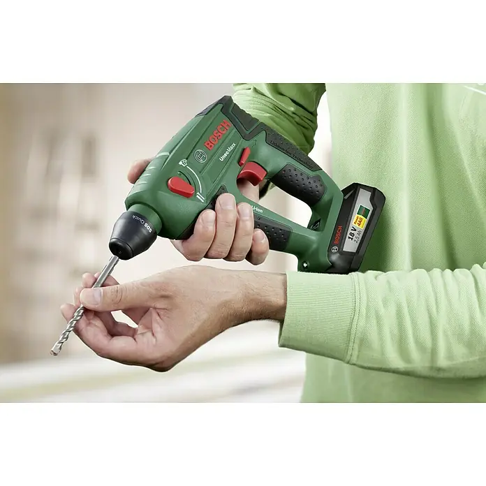 Bosch Power for All 18V Martillo perforador de batería Uneo MAXX - 18 V, 1 batería, 0,6 J - Primer plano de un martillo perforador inalámbrico Bosch UneoMaxx con una broca insertada, sostenido por una persona con sudadera verde.