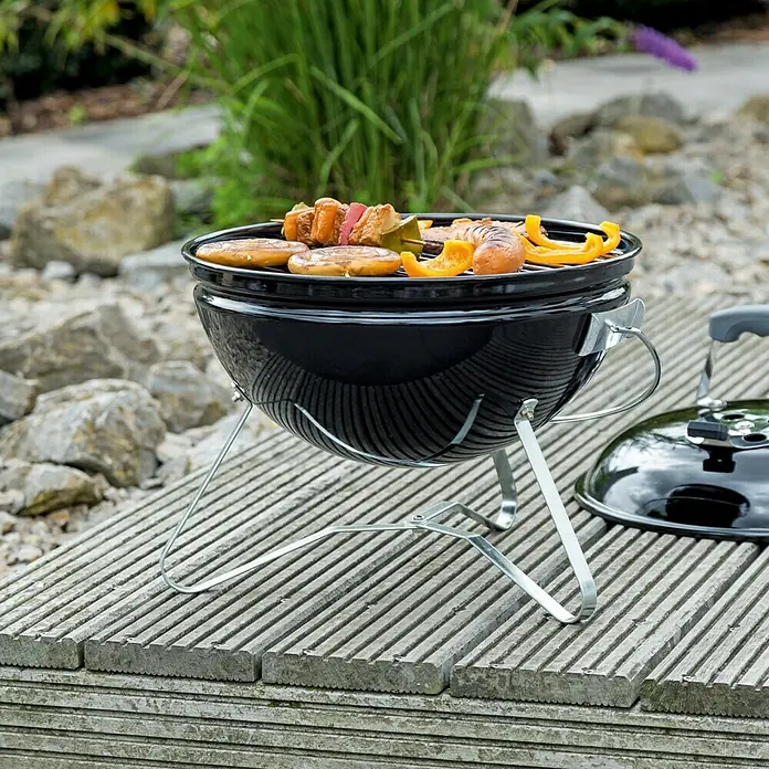 Kingstone Kugelgrill Cutie Pie - Durchmesser Grillfläche: 37 cm, Schwarz - Tragbarer Grill mit Grillgut, ideal für unterwegs. Der Grill steht auf einem Holzuntergrund und ist bereit für ein Barbecue.