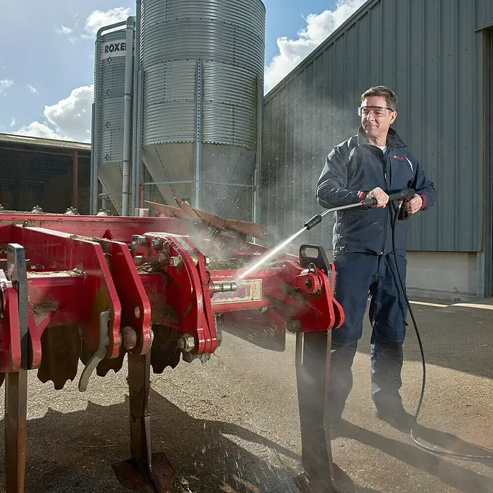 Bosch Professional Hochdruckreiniger GHP 5-55 - 130 bar, 2.200 W, Fördermenge: 520 l/h - Ein Mann reinigt mit einem Hochdruckreiniger ein rotes Landwirtschaftsgerät, im Hintergrund Silos und ein Gebäude.