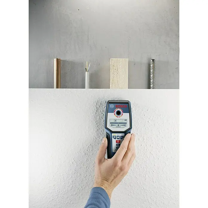 Bosch Professional Detector GMS 120 - Profundidad de detección: Máx. 120 mm de acero, Tiempo de funcionamiento: 5 h - Un operario sujetando un escáner de pared Bosch GMS 120 Professional contra una pared blanca texturizada.