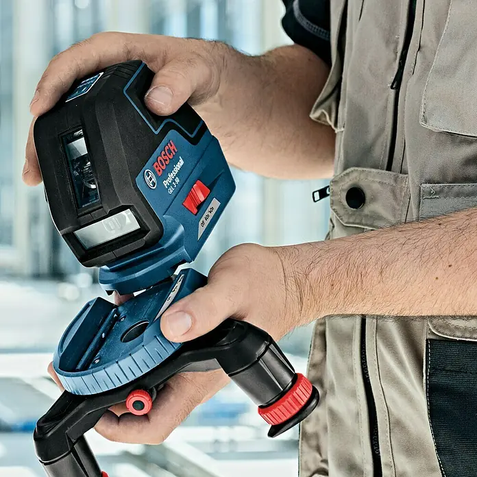 Bosch Professional Láser de línea GLL 3-50 - Zona de trabajo: 50 m (con receptor), 5 pzs. - Un hombre sostiene un láser de líneas Bosch GLI 3-30 Professional en sus manos, montándolo en un trípode. Ideal para tareas de alineación precisa.