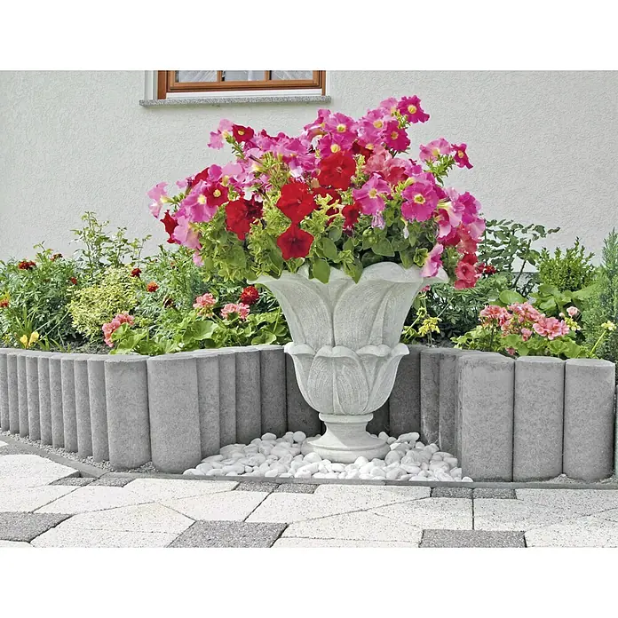 EHL Verbundpalisade - Ø x H: 10 x 60 cm, Grau, Beton - Blütenpracht in Vase: Üppige Blumen in Rot- und Pinktönen, präsentiert in einer eleganten, grauen Vase, umgeben von weißen Steinen und Pflastersteinen.