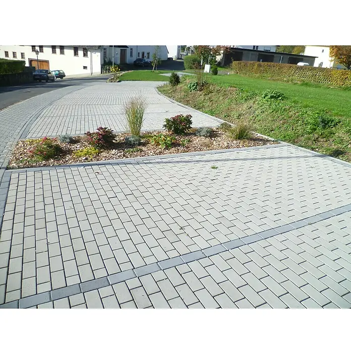 EHL Pflasterstein Drän - Grau, 20 x 10 x 8 cm, Rechteckig - Hier sind Pflastersteine zu sehen, die einen gepflasterten Bereich mit einem Blumenbeet in einer Wohngegend bilden.