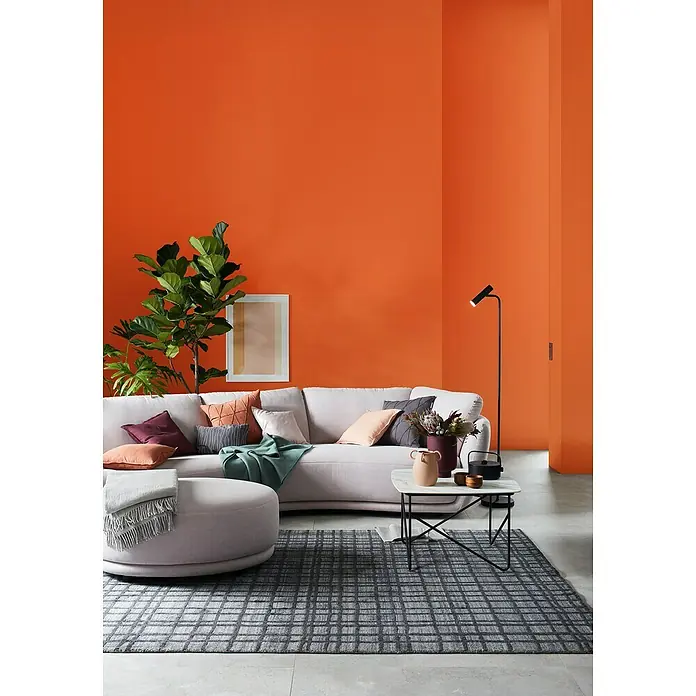 SCHÖNER WOHNEN-Farbe Wandfarbe Trendfarbe - Aperitivo, Matt, 1 l, Konservierungsmittelfrei - Wohnzimmer mit orangefarbener Wand, grauem Teppich, Sofa mit Kissen, Ottomane, Tisch und Stehlampe.