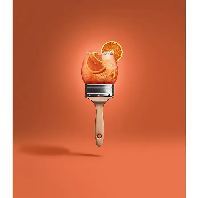 SCHÖNER WOHNEN-Farbe Wandfarbe Trendfarbe - Aperitivo, Matt, 1 l, Konservierungsmittelfrei - Abbildung eines orangefarbenen Cocktails mit Eis und Orangenscheiben auf einem Pinsel vor einem orangefarbenen Hintergrund.