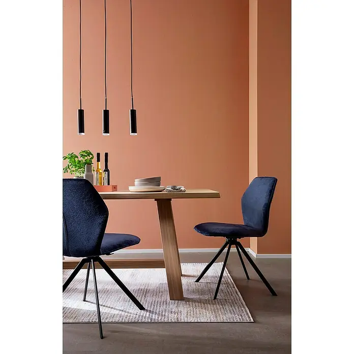 SCHÖNER WOHNEN-Farbe Wandfarbe Trendfarbe - Arizona, Matt, 1 l, Konservierungsmittelfrei - Esszimmer mit Holztisch, blauen Stühlen und drei schwarzen Hängelampen. Der Raum ist in einem warmen Orangeton gehalten.