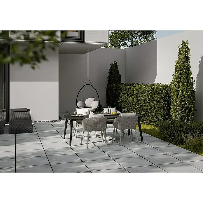 Terrassenfliese Dimension - 59,7 x 59,7 x 2 cm, Grau, Matt - Ein einladender Außenbereich mit einem eleganten Esstisch-Set, einem hängenden Stuhl und stilvollen Lounge-Möbeln, umgeben von üppigem Grün.